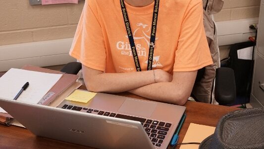 Teacher Lorien Gilbert sits at her desk with her freshly, shaven head