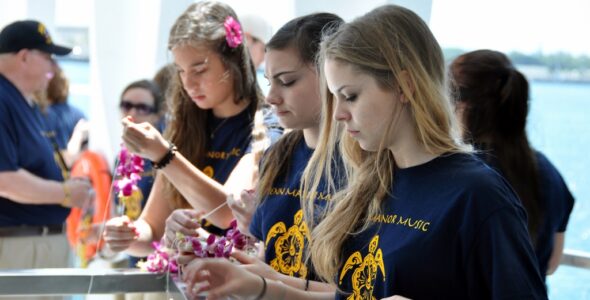 Students Johanna Dunford-Groves, Liz Schettler and Lavinia Hess, from left, drop flowers from their lei necklaces in the water at the USS Arizona .