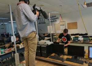 Cameraman Andrew Johnson captures Lance Brubaker at work in the tech support helpdesk.