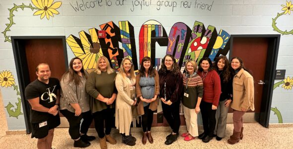 Teachers and other staff members standing in front of a "welcome" sign