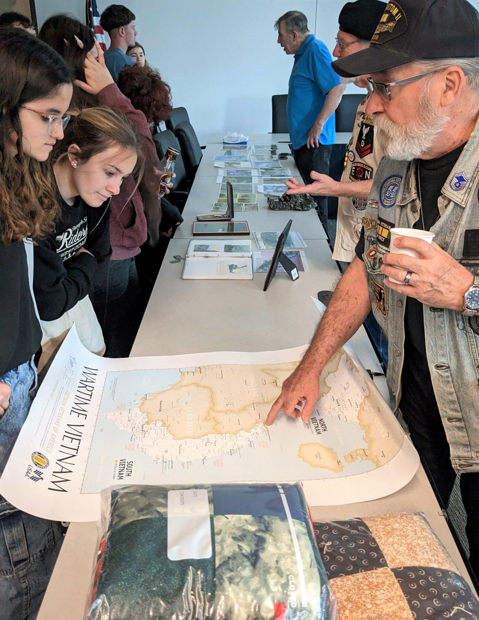 A veteran points to a map of Vietnam as two students look on.