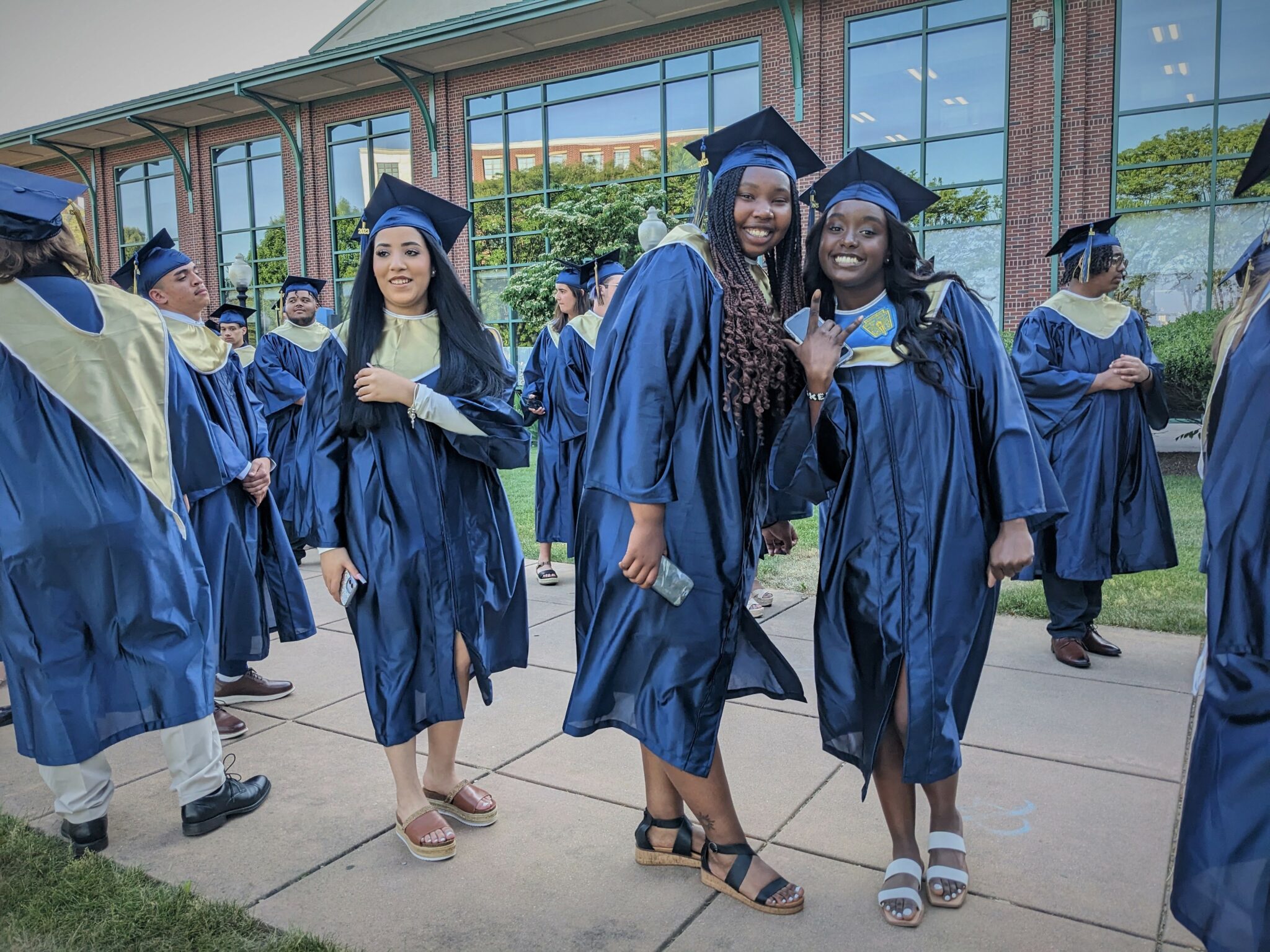 Photo of three graduates posing while waiting in line outside to get into commencement