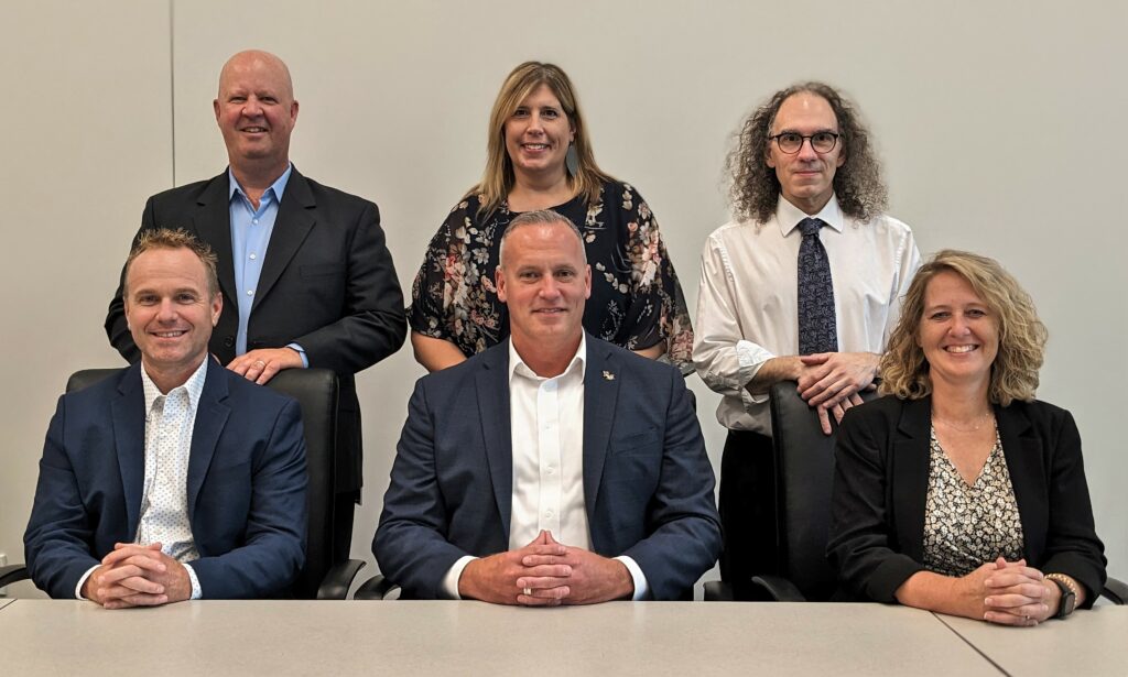 Group photo of six leadership team members at a table.