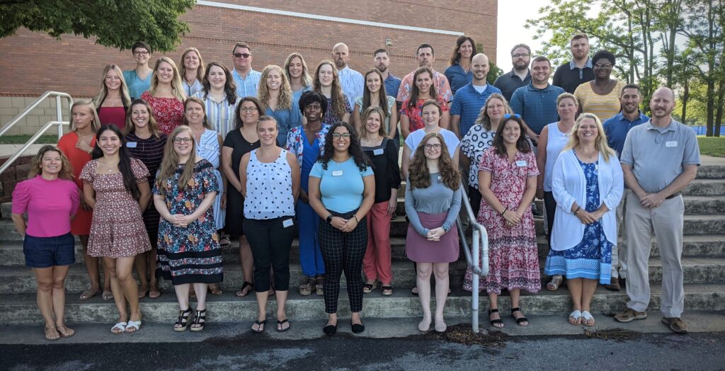 A group of 30 new teachers standing in front of a school