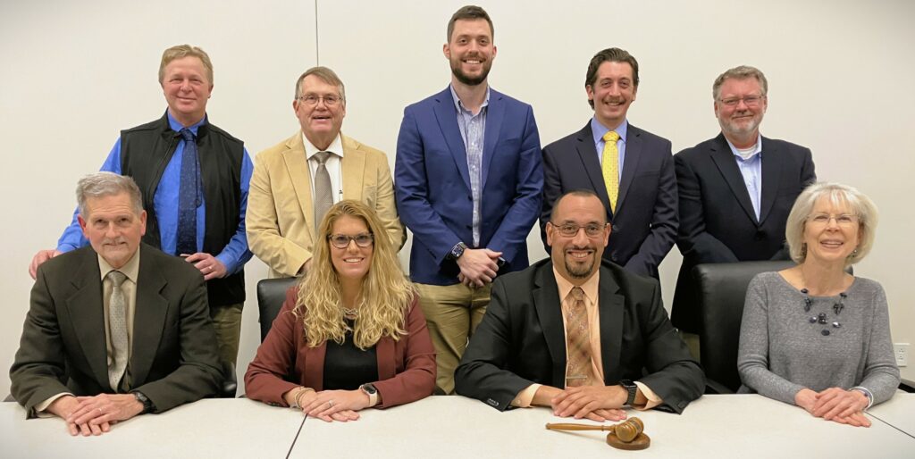 Nine school board members posing at table.