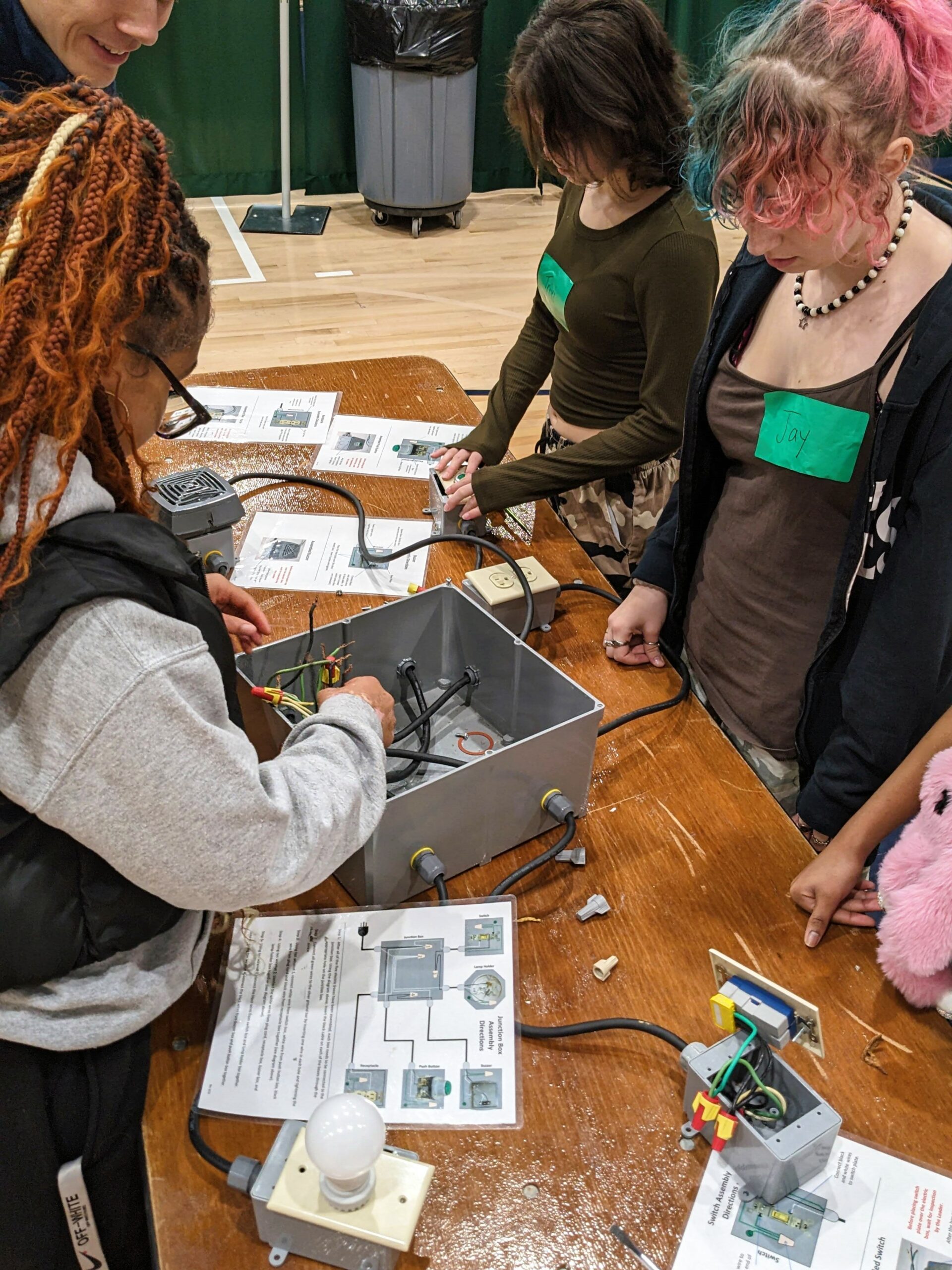 Three students attempt to connect wires to activate a light.