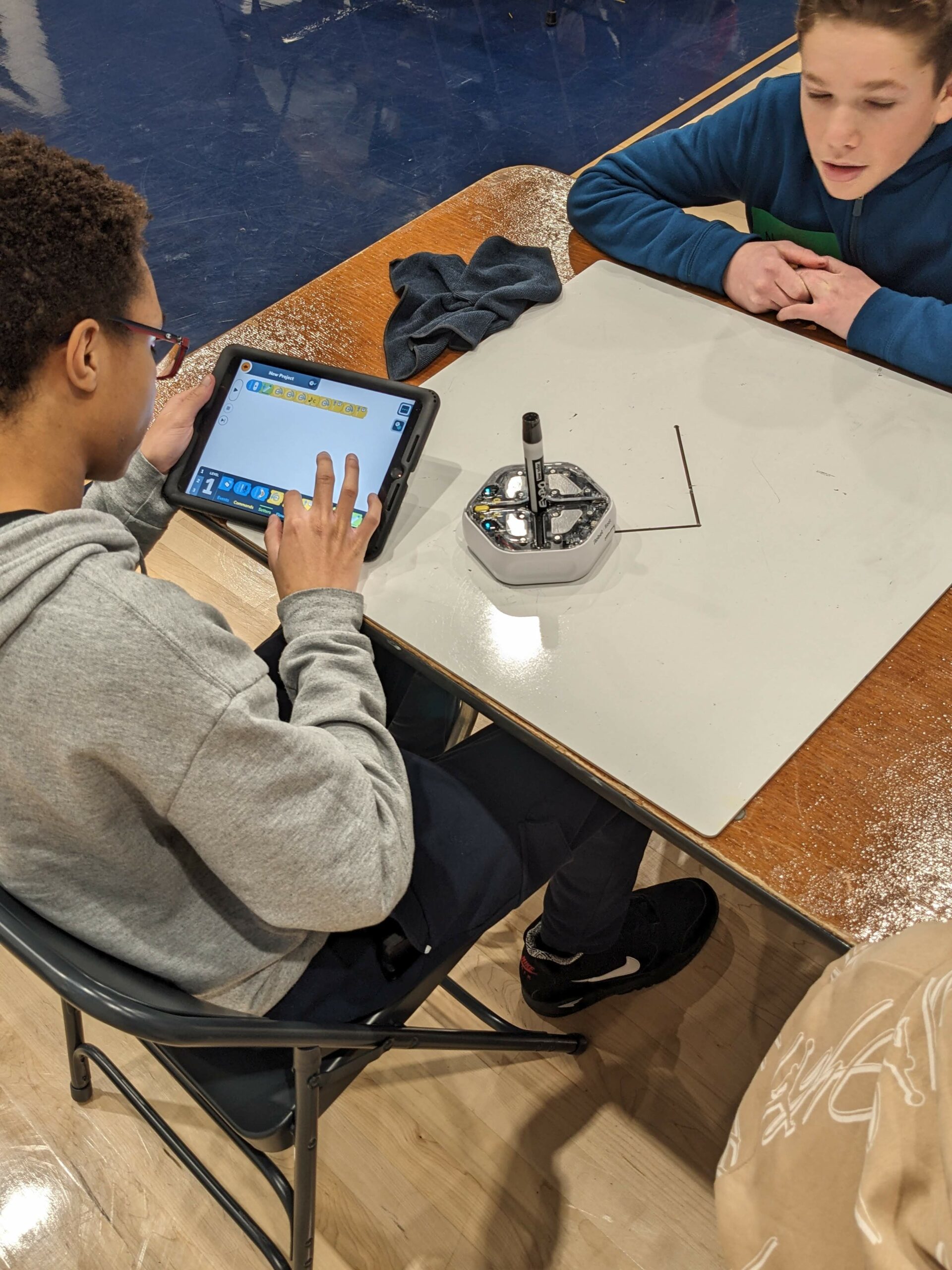 Two students program a robot to draw a design on a whiteboard.