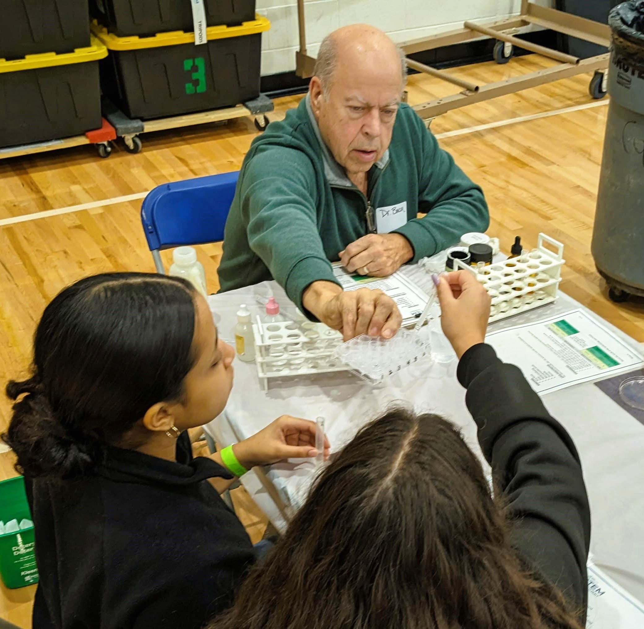 Two students and a volunteer exchange samples in test tubes.