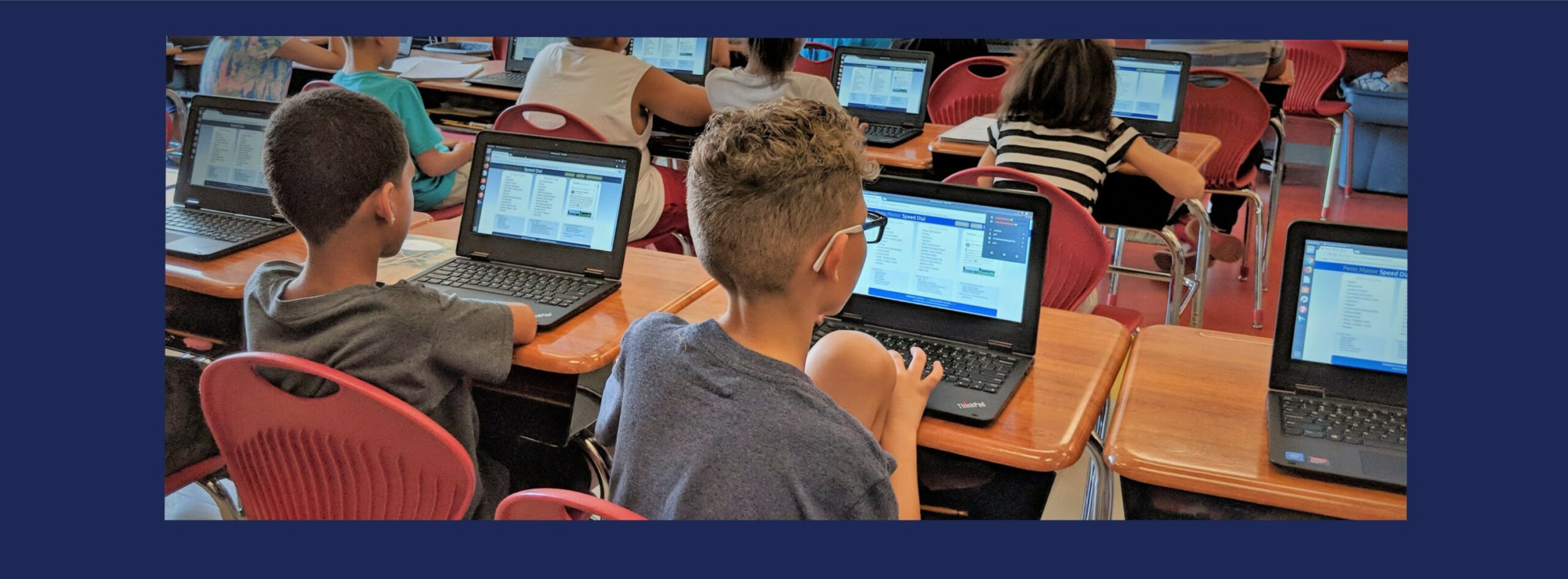 Several students working on laptops at desks in a classroom.