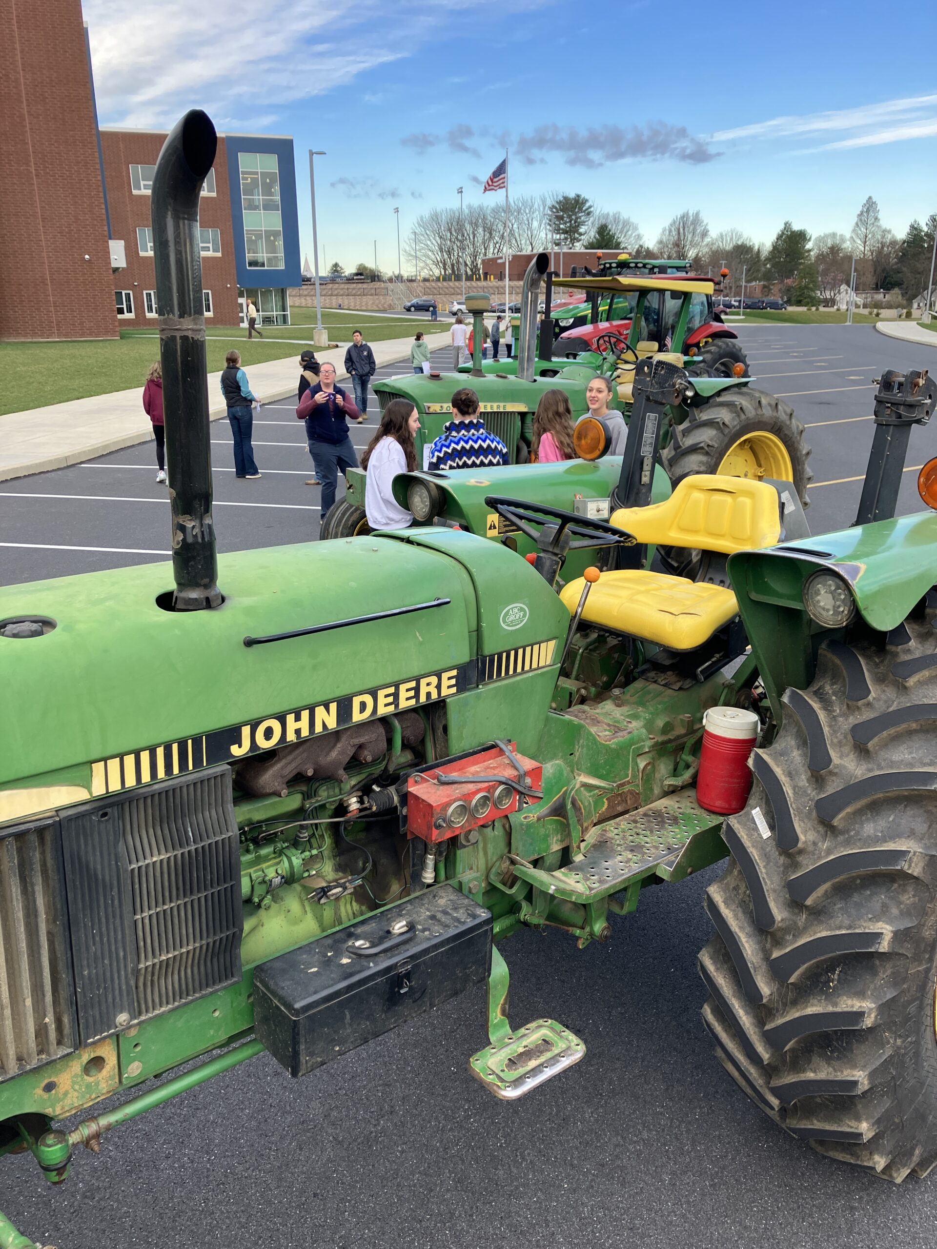 Students and teachers walk among tractors in the school parking lot.