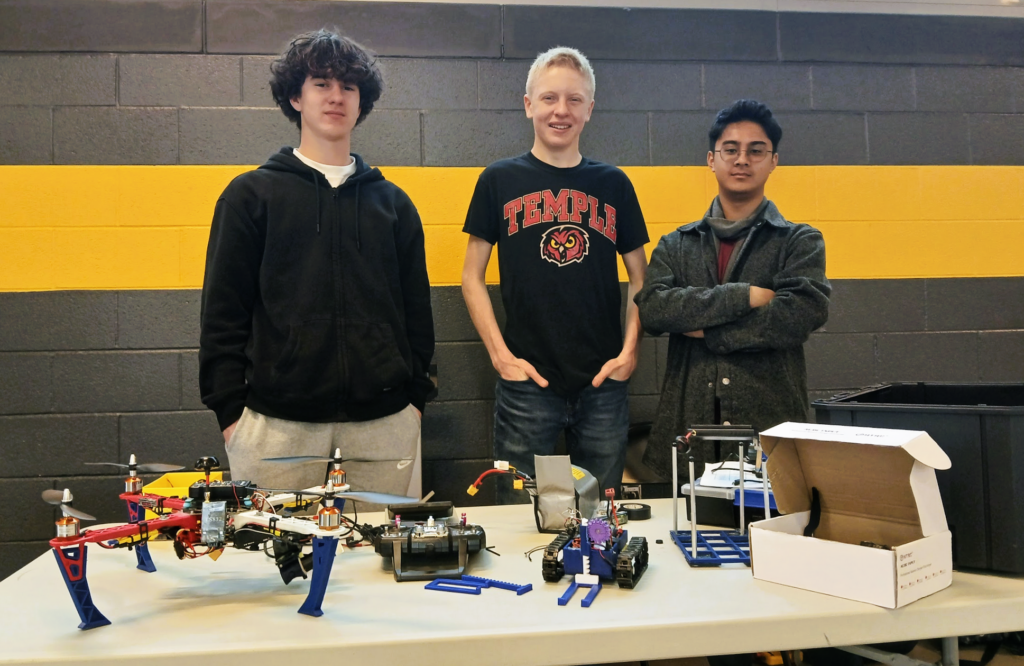 Three robotics team members with drone, rover and other gear.