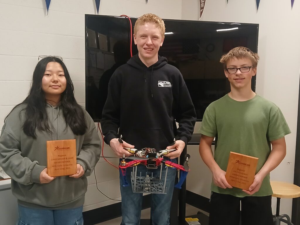 Three robotics team members holding their trophies and a drone.