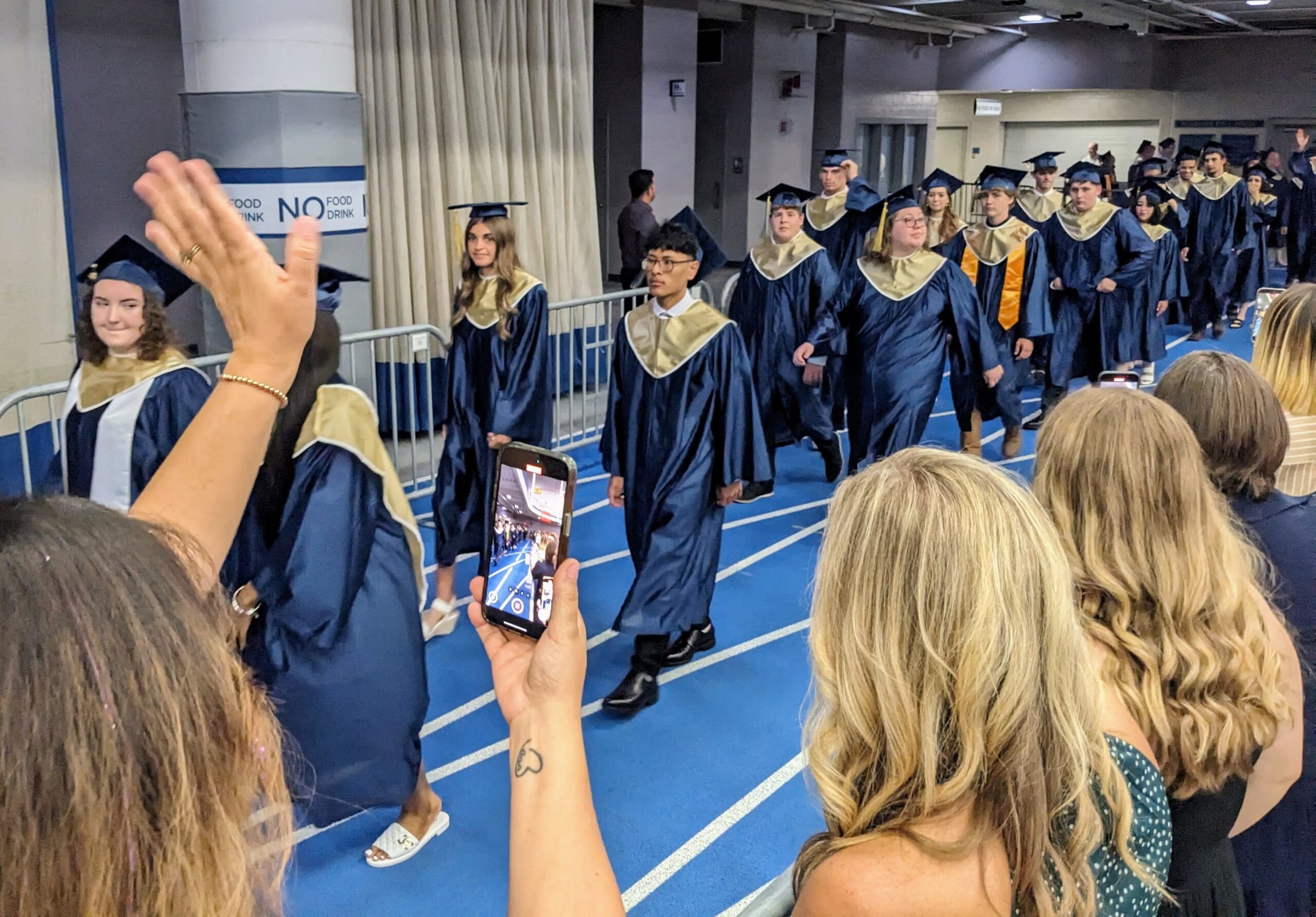 Family members gesture to graduates as they walk by.