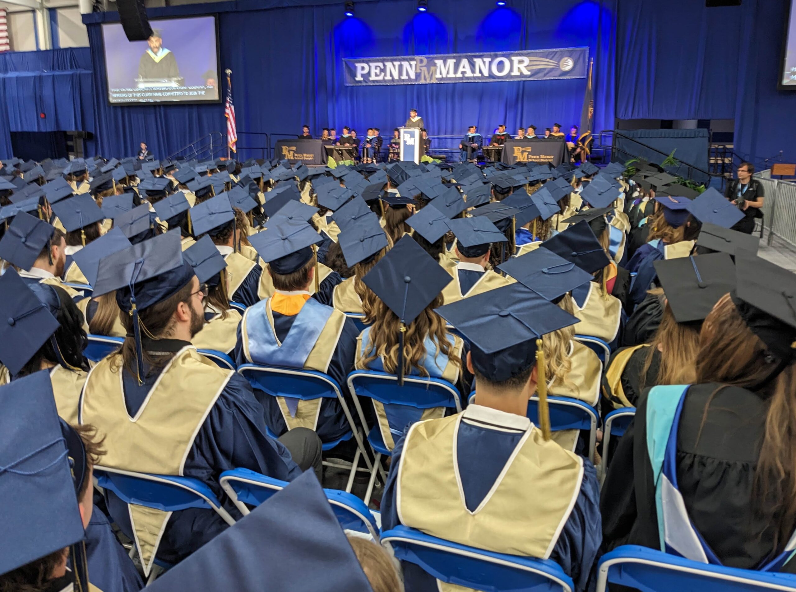Graduates in rows with stage visible in the distance.